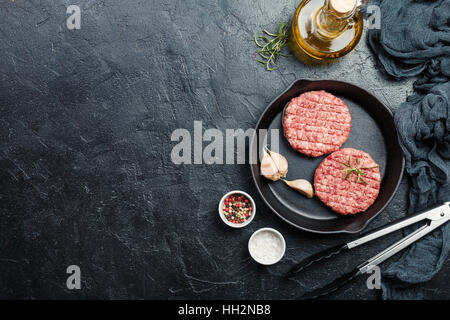 Materie hamburger - cotolette da materia organica a base di carne di manzo con aglio e rosmarino in una padella su sfondo nero, vista dall'alto con spazio di copia Foto Stock