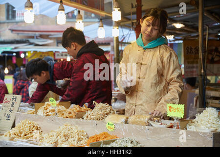 Taipei, Taiwan. 15 gennaio, 2017. Un fornitore di vari pesci secchi e calamari guarda verso di lei in magazzino. Gli studenti hanno spesso prendere lavori temporanei manning i banchi del mercato. Per le due settimane che precedono il nuovo anno lunare vacanza, una vacanza speciale mercato è impostato lungo Taipei Dihua della St per la gente per fare scorta di snack e prelibatezze. Credito: Craig Ferguson/ZUMA filo/Alamy Live News Foto Stock