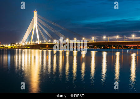 Riga, Lettonia. Vista panoramica di Vansu Cable-Stayed Ponte In brillante illuminazione notturna oltre il Fiume Daugava, Western Dvina e colore le riflessioni sulla Wat Foto Stock