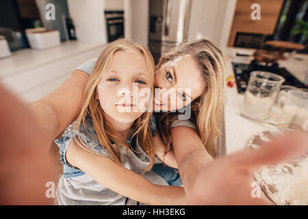 Donna felice e ragazza tenendo un selfie. Sia in cucina con la madre in possesso di un telefono cellulare. Foto Stock