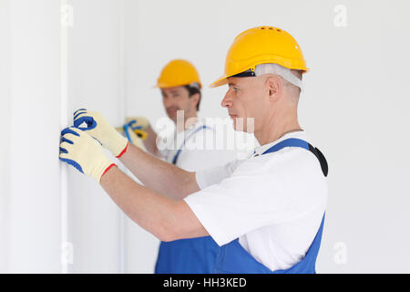 Gli uomini in uniforme e hardhats parete di misurazione con nastro Foto Stock