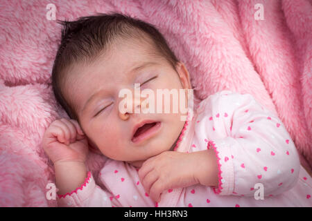 A meno di tre settimane di età simpatico baby girl, dormire con la bocca aperta su una coperta rosa. Nouveau-né dormienti bouche ouverte. Foto Stock