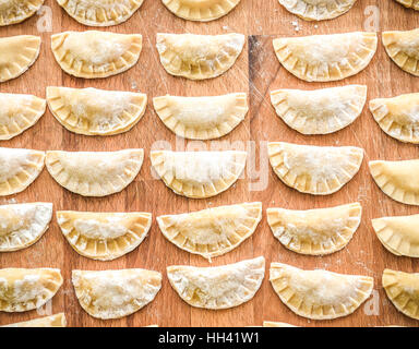 Realizzazione di gnocchi fatti in casa la pasticceria tortellini o ravioli. Modello per la pasta fatta in casa ripiena di carne. Preparazione di pasti organici su una scrivania in legno. Foto Stock