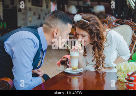 La giovane coppia amorevole beve un cappuccino da un vetro attraverso tubuli. Nozze Foto Stock