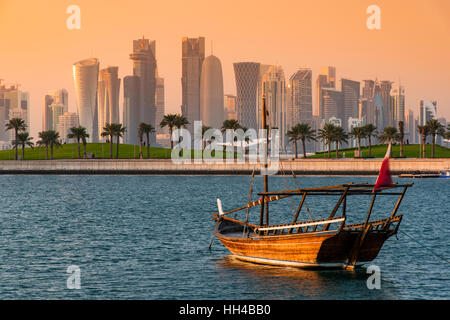 Dhow tradizionale imbarcazione a vela con il settore finanziario skyline dietro al tramonto, Doha, Qatar Foto Stock