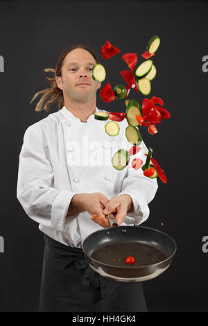 Foto di un giovane chef con Dreadlocks nel lanciare un trito di verdure in aria da una padella. Foto Stock