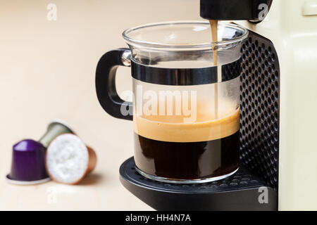 A singolo che serve caffe macchina eroga caffè espresso in un bicchiere di vetro con capsule di caffè in background Foto Stock