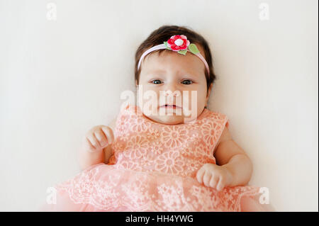 Carino bambina con la faccia triste giace su una coltre bianca Foto Stock