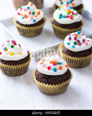 In casa tortini di cioccolato con glassa di bianco su bianco sullo sfondo di legno Foto Stock