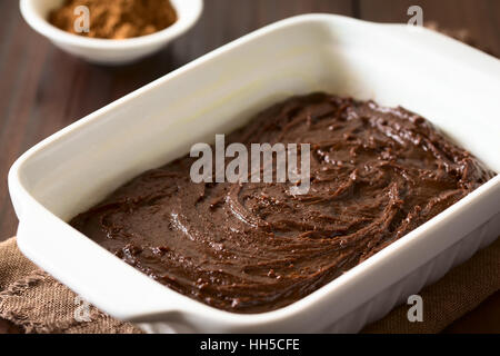 In casa di base brownie o torta al cioccolato in pasta imburrato e infarinato teglia, fotografato in legno scuro con luce naturale Foto Stock
