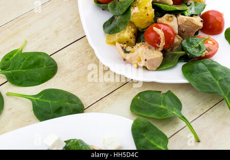 Guarnito con taglio feta insalata di spinaci, pollo, pomodori ciliegini e arancione sulla piastra bianca Foto Stock