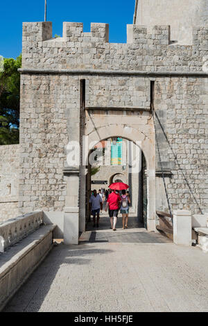 Un giovane con un ombrello rosso entrano in Dubrovnik, Croazia Città Vecchia attraverso la storica città di pietra gate. Foto Stock