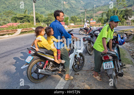 Padre il trasporto di tre bambini, fermo lungo la strada rurale, avente una conversazione dal mercato degli agricoltori, Yamaha Sirius RC motociclo. Foto Stock