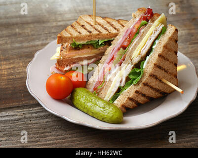 Foto di un club sandwich realizzati con la Turchia, pancetta, prosciutto, pomodoro, formaggio, lattuga e guarnito con una salamoia e due pomodori ciliegia. Foto Stock