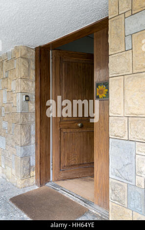 La metà anteriore aperta della porta di legno a mattoni di pietra parete colorata e di un marrone zerbino Foto Stock