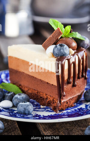 Pezzo di tre deliziosa mousse al cioccolato torta decorata con mirtilli freschi, menta e caramelle Foto Stock