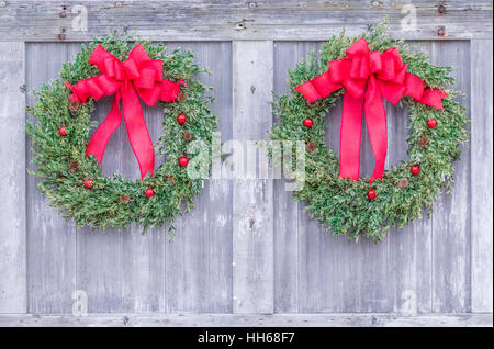 Due luminose e festa di Natale ghirlande appese a fianco a fianco su una porta del granaio Foto Stock