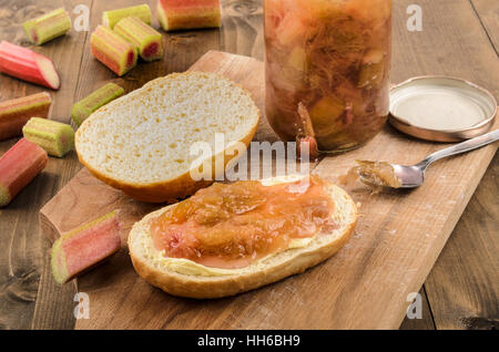 Metà panino, guarnita con fatti in casa di rabarbaro marmellata su una tavola di legno Foto Stock