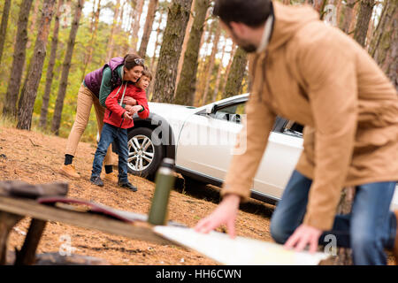 Giovane uomo che guarda la mappa e la donna con il bambino in piedi vicino al bianco auto nella foresta di autunno Foto Stock