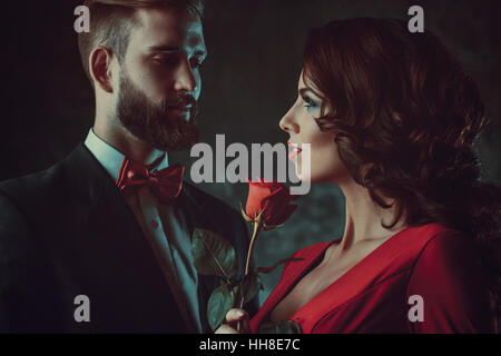 Giovane ed elegante giovane. Woman in Red Rose di contenimento e alla ricerca sull'uomo. Focus sulla donna. Vintage stile pellicola a colori. Foto Stock