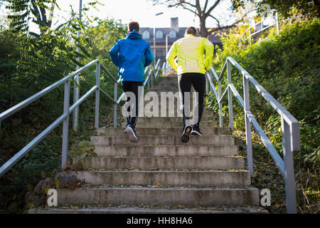 Due atleti in esecuzione su scale in autunno soleggiato, in vista posteriore Foto Stock