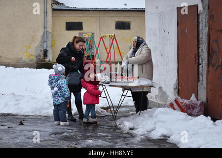 Giovane madre di lecca-lecca di acquisto per i suoi due bambini piccoli da una vecchia signora nella scuola del villaggio cantiere durante la celebrazione Surva Foto Stock