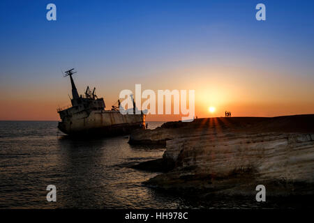 La gente al tramonto guardando una nave arenata da una roccia Foto Stock