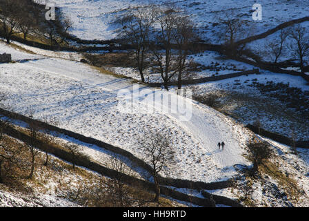 Due figure che camminano attraverso un paesaggio invernale e innevato illuminato ed evidenziato da un basso sole pomeridiano sdraiato vicino a Malham nello Yorkshire Foto Stock