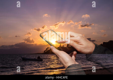 Doppia esposizione della donna mano touch screen smart phone su sunrise sulla spiaggia Foto Stock