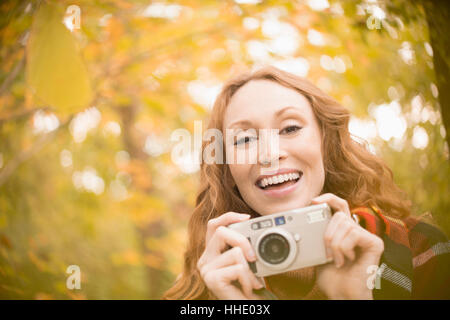 Ritratto di donna entusiasta con fotocamera digitale sotto gli alberi di autunno Foto Stock