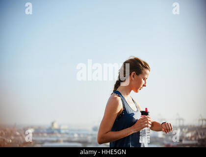 Runner con una bottiglia d'acqua controllo smart watch tracker fitness sotto sunny bleu sky Foto Stock