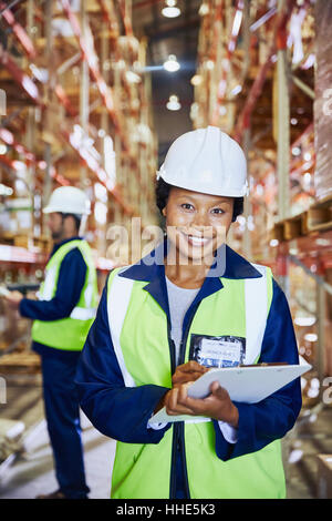 Portrait confident female manager with clipboard in distribution warehouse Foto Stock