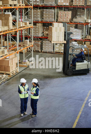 Il carrello elevatore a forche e i lavoratori riuniti in magazzino di distribuzione Foto Stock