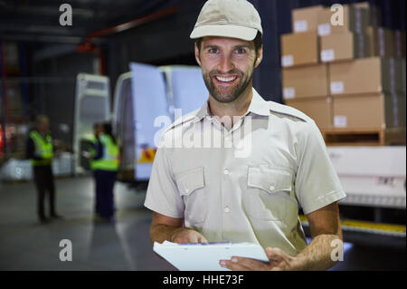 Ritratto sorridente camionista lavoratore con appunti nel magazzino di distribuzione per dock di caricamento Foto Stock