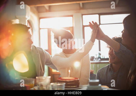 Giovani amici festeggia il compleanno con torta e candela ad alta fiving Foto Stock