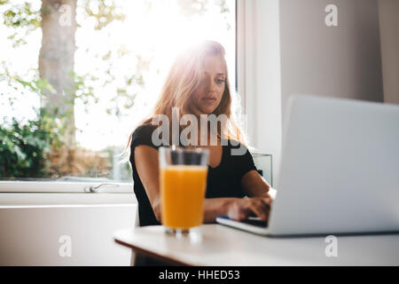 Tiro al coperto del lavoro femminile sul laptop. Donna in mattinata in cucina e utilizzando il computer portatile. Foto Stock