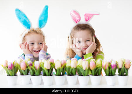 Dei bambini felici celebrare la Pasqua in casa. Un ragazzo e una ragazza indossando orecchie di coniglietto godendo di ricerca delle uova. I bambini a giocare con i colori delle uova Foto Stock