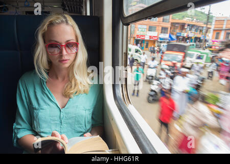 Bionda donna caucasica la lettura di un libro sul treno dalla finestra. Foto Stock