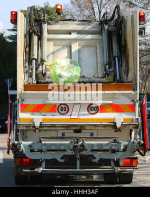 Grande nettezza urbana camion durante la raccolta dei rifiuti solidi per la città e una grande busta gialla di immondizia Foto Stock