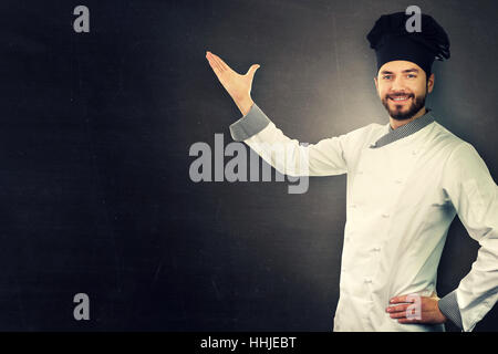 Giovani chef sorridente in uniforme bianco su nero con spazio di copia Foto Stock