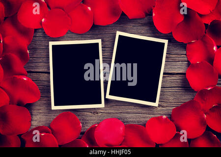 Il giorno di San Valentino blank foto cornici di legno su sfondo rosso e petali di rose. Dai toni rétro Foto Stock