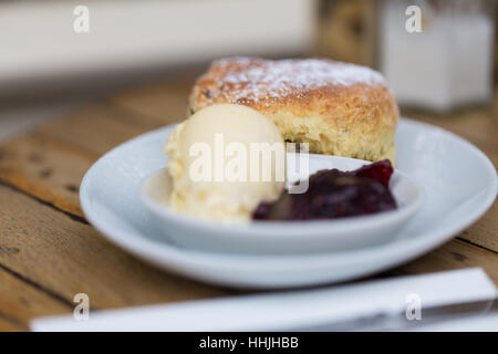 Home reso scone spolverato di zucchero a velo, clotted cream e marmellata sulle stoviglie bianco sul tavolo di legno Foto Stock