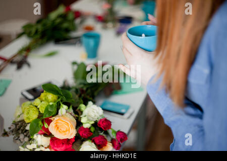 Workshop fioraio, rendendo mazzi di fiori e decorazioni. Donna in appoggio con la tazza di tè in mani. Soft focus Foto Stock