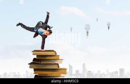 Giovane imprenditore allegro facendo handstand sulla pila di libri Foto Stock