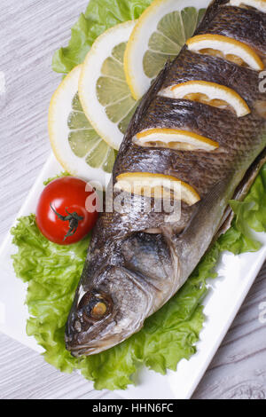 Branzino grigliato con limone, lattuga e pomodoro ciliegino close-up su una piastra verticale. vista superiore Foto Stock
