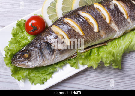 Branzino grigliato con limone, lattuga e pomodoro ciliegino close-up su una piastra orizzontale. vista superiore Foto Stock