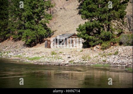 Abbandonata cabina con dipendenza, circondato da alberi, sulle rive del fiume di salmoni a dente di sega la gamma della montagna Foto Stock