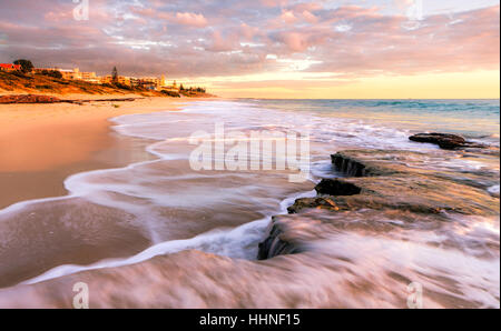 Tramonto a nord Cottesloe Beach con un'onda rotolando su di un ripiano di pietra calcarea. Perth, Australia Foto Stock