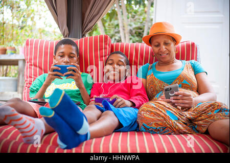 Madre nera e figli gemelli utilizzando i telefoni cellulari all'aperto Foto Stock