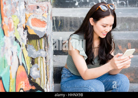 Thai sorridente donna seduta su scala urbana sms sul cellulare Foto Stock